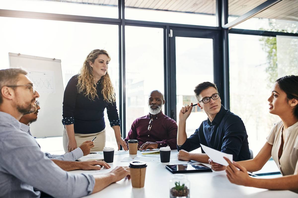 A team around a meeting table with notes in front of them, one colleague standing to lead the conversation
